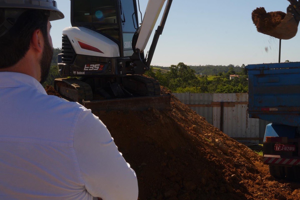 Prancheta com projeto de obra comercial sobre mesa de escritório de engenharia, com planta baixa, réguas e capacete ao lado, ambiente da EZA Engenharia em Criciúma